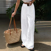 Person wearing white lace pants holding a woven bag outdoors.